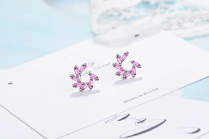 Close-up of silver stud earrings with pink rectangle crystals in a circular pattern