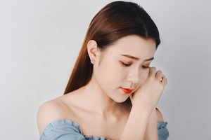 Detailed view of a woman wearing minimalist pink flower zircon stud earrings on a white background