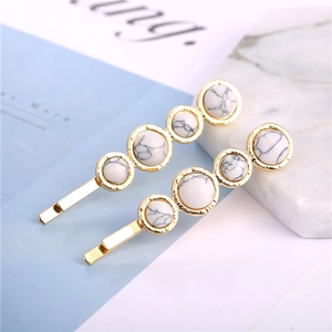 Close-up of golden hairpins with marble stones on a minimalist decorative background