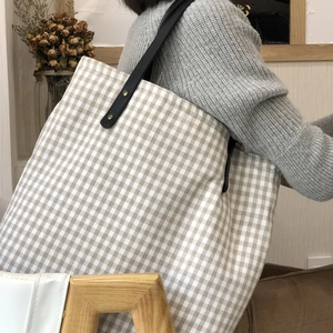 Detail of light brown checkered tote bag with black leather strap and gold rivets