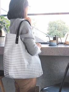 Detail of grey plaid fabric tote bag with black leather handle and rivet accents