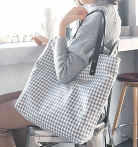 Detail of blue plaid fabric tote bag with black leather shoulder straps and metal rivets