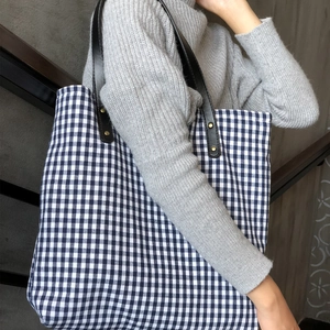 Detail of checkered canvas tote bag with black leather straps and metal rivet fasteners