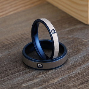 Titanium steel minimalist blue matte couple rings with single diamond on wood surface