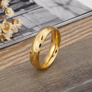 Bague vague minimaliste en acier titane doré posée sur une surface en bois avec fleurs séchées