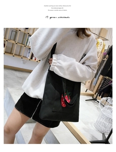 Detail of black canvas tote bag with red strawberry embroidery on model in casual setting