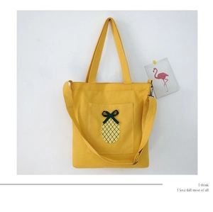 Detail showing a yellow canvas tote with a pineapple patch and a green ribbon bow