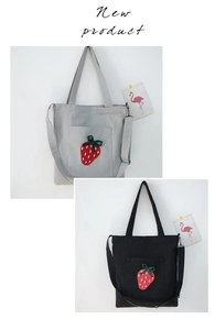 Detail of grey and black canvas tote bags featuring vibrant strawberry embroidery