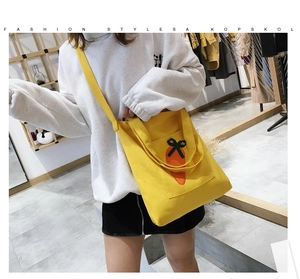 Detail of yellow canvas shoulder bag with a cute carrot patch and a green bow accent