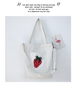 Detail showing red strawberry embroidery and green ribbon bow on white canvas tote bag