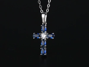 Macro shot of silver cross pendant with blue oval zircons and center crystal on black background