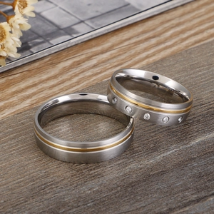 Polished stainless steel couple rings with gold inlay and zircon on wooden surface