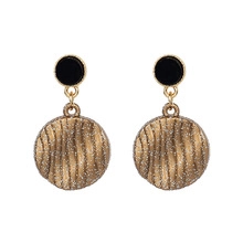 Détail de boucles d'oreilles bohèmes dorées avec puces noires et finitions ondulées