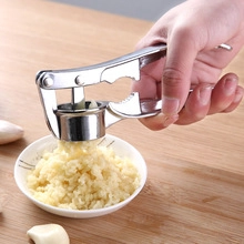 Manual garlic press mincing fresh cloves into a small bowl over a wooden table