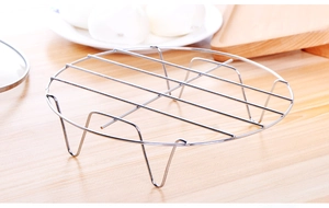 Detail of a round stainless steel steaming rack with four legs on a wooden table
