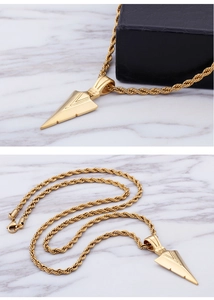 Détail du pendentif flèche dorée avec chaîne torsadée sur marbre et boîte à bijoux