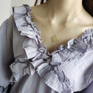 Close-up of a 925 sterling silver gold-plated coin necklace on a lavender blouse