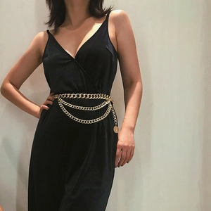 Detail of a multi-layer gold metal waist chain with a round pendant on a black outfit