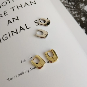 Polished silver and gold U-shaped geometric earrings set on a minimalist white book