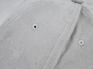 Detail of grey suede baseball cap with reinforced stitching and embroidered eyelets