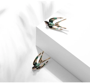 Detailed macro view of flying swallow brooches with green enamel and crystal inlay