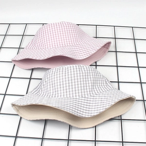 Detail view of double-sided checkered bucket hats in pink and grey on mesh surface