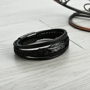 Close-up of black multilayer leather bracelet with a black steel feather charm on wood