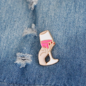 Creative hand holding wine glass enamel pin on blue denim fabric background