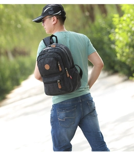 Outdoor view of a black canvas backpack featuring multiple pockets and durable shoulder straps