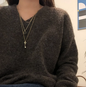 Close-up of a triple layered gold necklace with a key pendant worn on a grey sweater