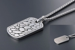 Detailed macro view of pebble-textured silver military pendant with a braided steel chain