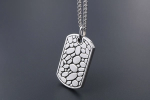 Detail of silver titanium military tag pendant with textured pebble surface and braided chain