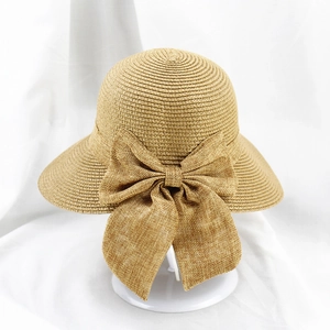 Détail d'un chapeau de paille beige avec un grand nœud élégant sur support blanc