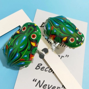 Close-up of two vintage wind-up tin frogs with colorful patterns on a blue background