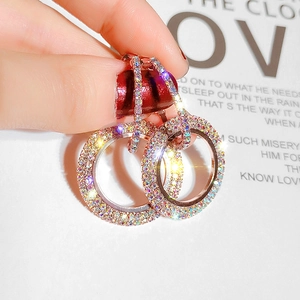 Macro shot of rose gold hoop earrings with multi-color crystals held over a magazine
