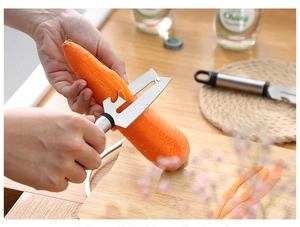 Action shot of a stainless steel peeler removing skin from a fresh carrot over a wooden board