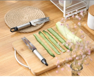 Detail view of a multifunctional stainless steel peeler slicing a fresh cucumber on wood