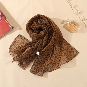 Detail of leopard print chiffon scarf layered with perfume bottle on beige background