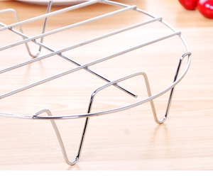 Macro shot of circular stainless steel steaming rack with three legs on wooden table