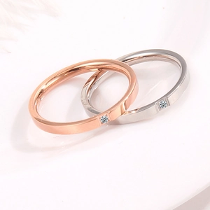 Minimalist rose gold and silver couple rings with single diamond inlay on white surface