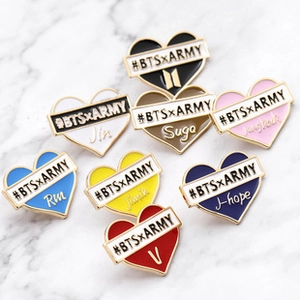 Detail of colorful heart enamel pins with gold borders and member names on marble surface