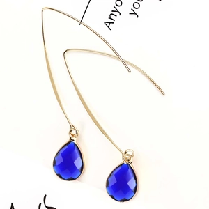Detailed close-up of dark blue teardrop crystal earrings with faceted gold hooks