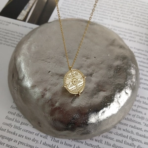 Close-up of golden coin necklace with eye relief detail on a vintage book background