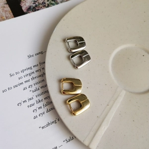 Detail shot of gold and silver U-shaped earrings on a white ceramic plate with a book