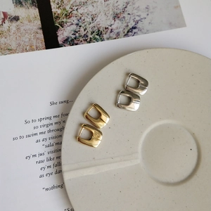 Macro shot of gold and silver geometric U-shaped earrings on a white ceramic plate