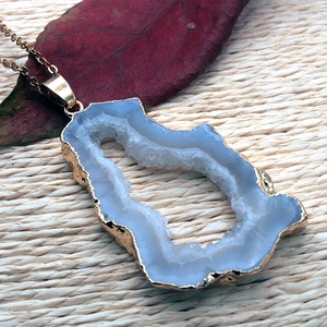 Detalle de colgante de geoda de ágata azul natural con borde dorado en fondo tejido