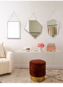 Detail of three geometric gold metal framed mirrors with slim hanging chains on a white wall
