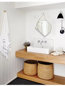Detail of a minimalist gold hexagonal wall mirror with hanging chain in a modern bathroom