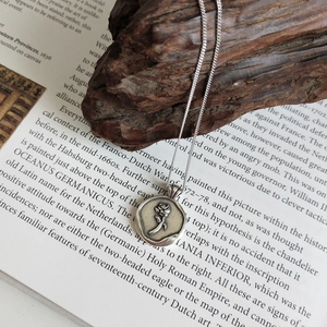 Detail of 925 silver necklace with rose seal pendant on vintage book background