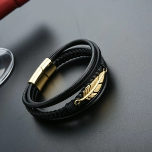 Macro detail of braided black leather bracelet with golden feather charm and magnetic clasp